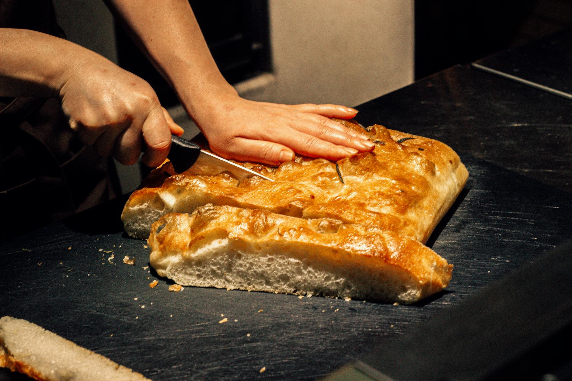 Krojenie prostokątnej domowej focaccii na ciemnym blacie