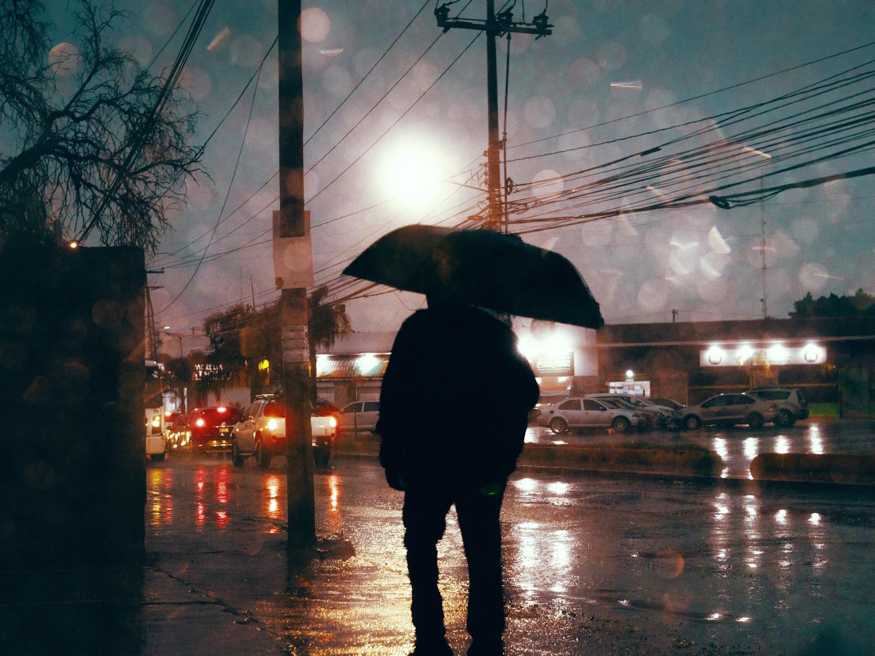 Sylwetka osoby z parasolem na deszczowej ulicy wieczorem