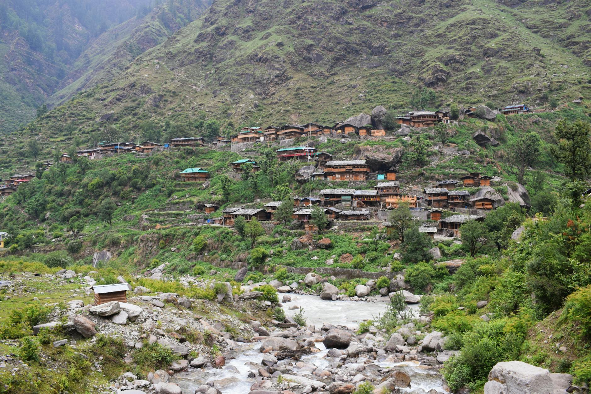 Górska wieś nad kamienistą rzeką otoczona zielonymi zboczami